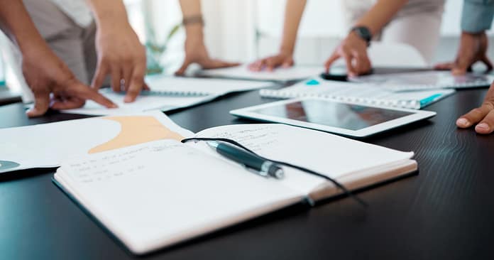 Closeup shot of a notebook on a table with businesspeople brainstorming in the background