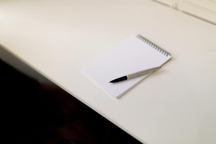 Notepad and pen placed on a white desk ready for writing ideas or notes