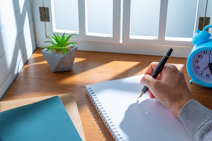 A hand is writing with a fountain pen on a blank notebook.