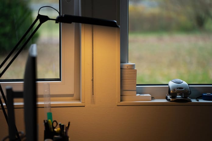 Minimal home office desk setup near window with modern lamp, pen holder, and computer screen showing workspace lighting arrangement, interior design balance, and productivity-oriented environment